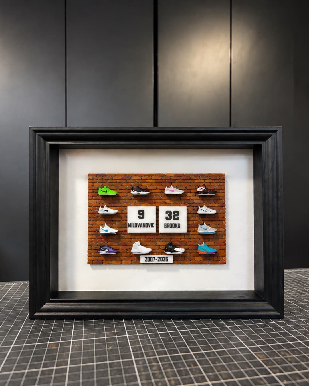 Framed brick wall of miniature basketball sneakers around two jersey plaques
