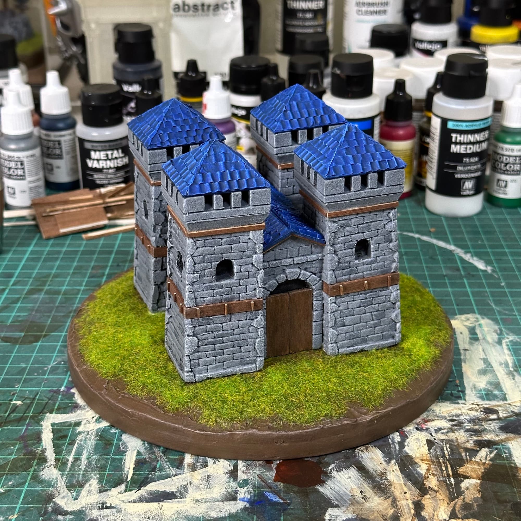 Hand-painted miniature stone castle with blue roofs on a grass base
