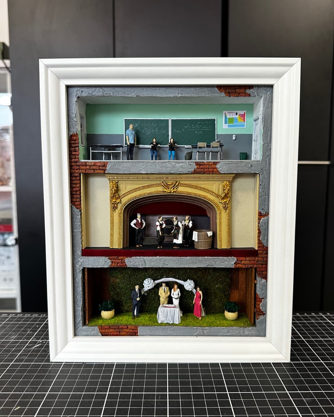 Framed three-level miniature with a classroom, a theatre stage and a garden wedding