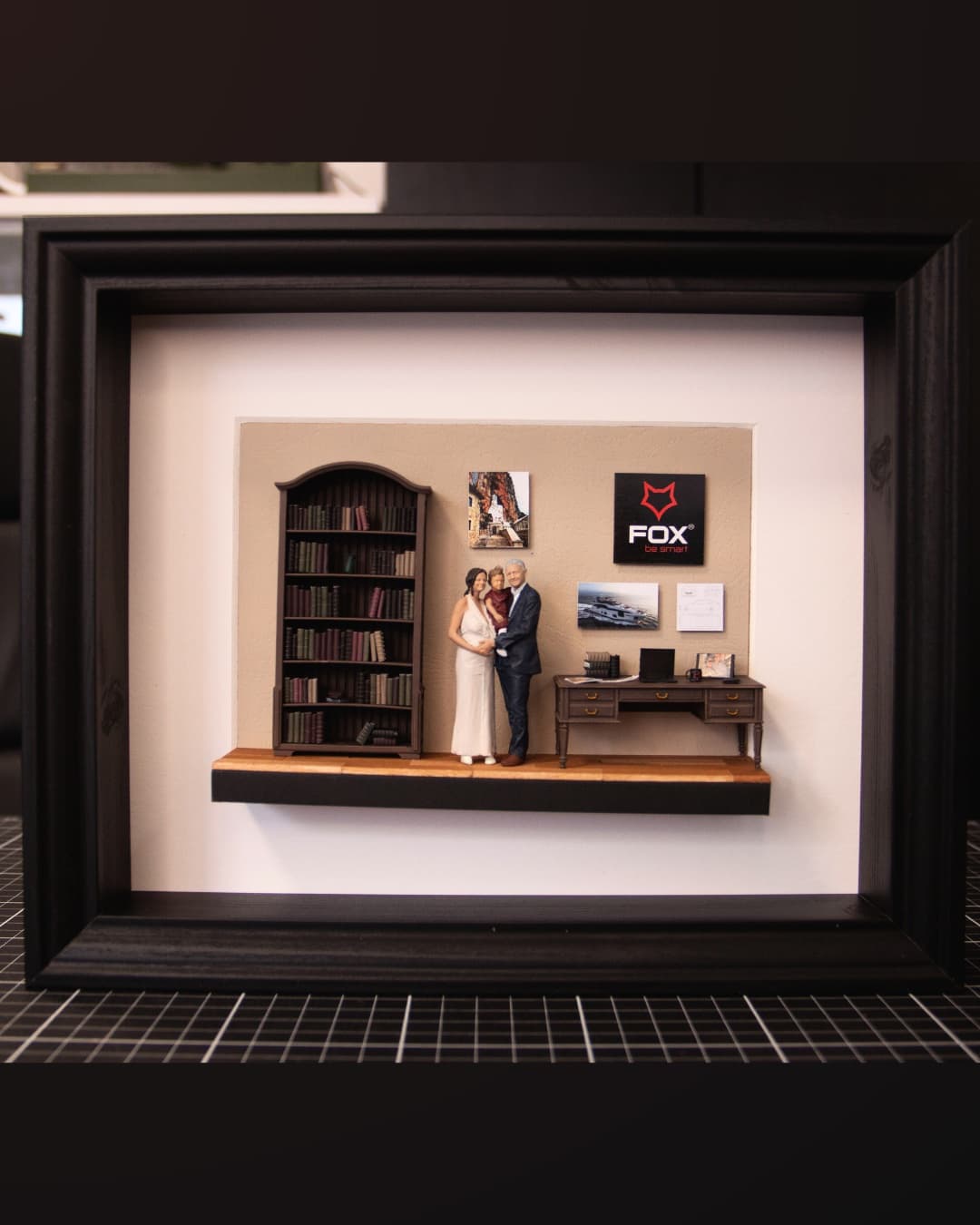 Framed miniature of a couple standing between a bookcase and a desk