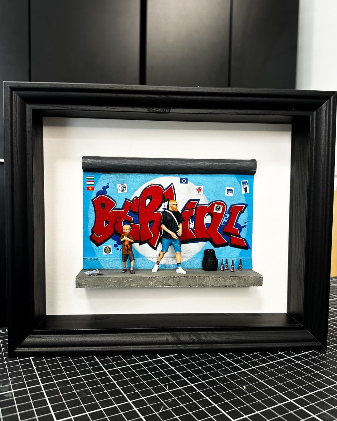 Framed miniature of a father and son in front of a red and blue graffiti wall