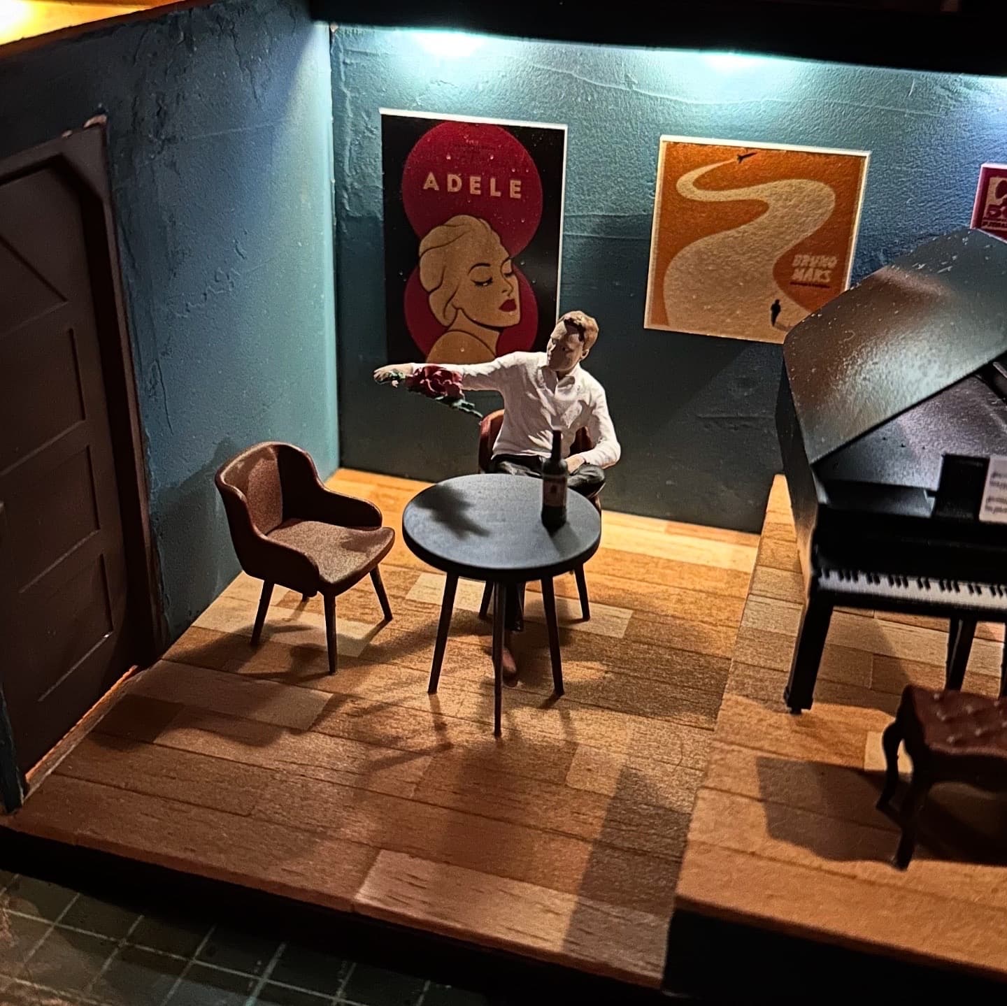 Miniature lounge with a figure at a round table under music posters