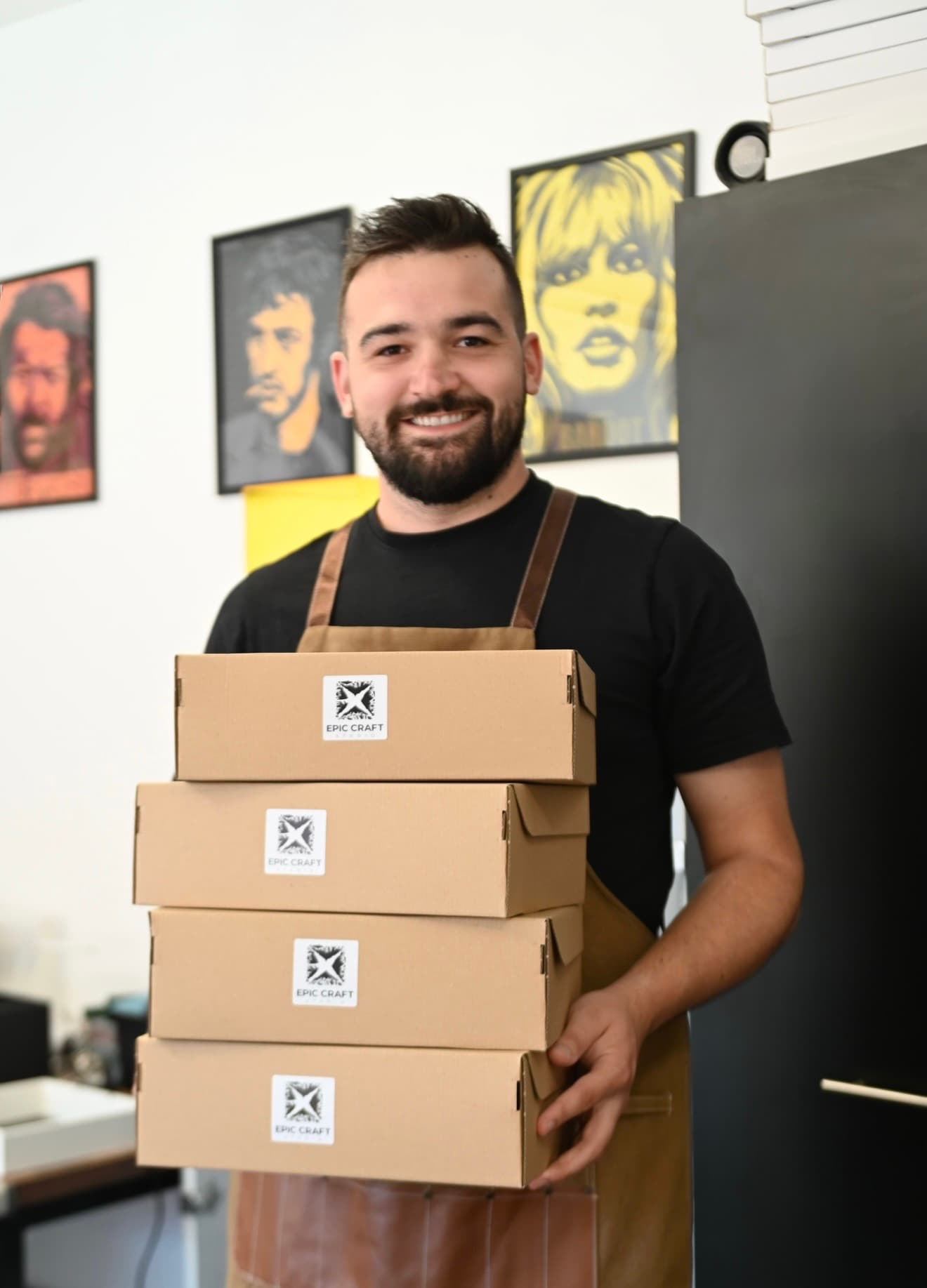 Lazar Stajčić, founder of Epic Craft Studio, in his workshop holding a stack of Epic Craft boxes