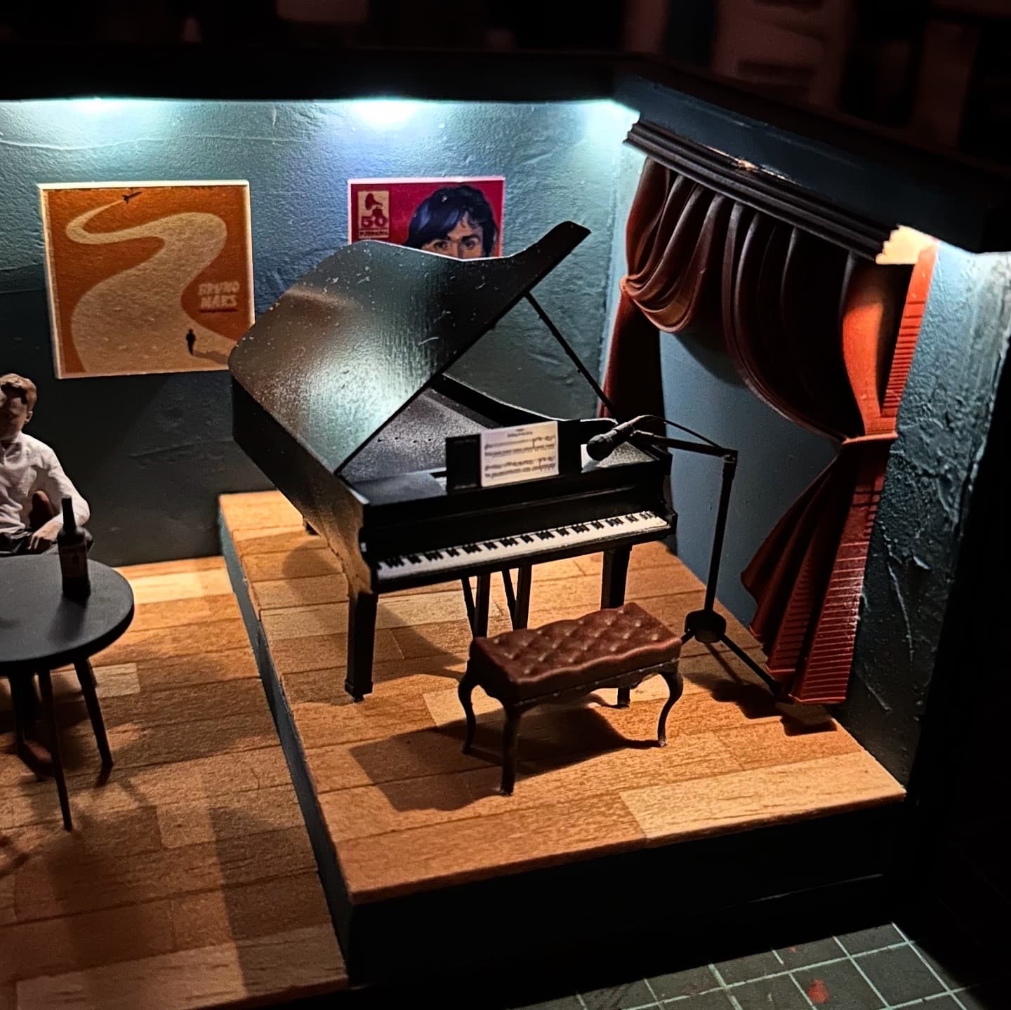Close-up of a miniature grand piano on a small stage with a red curtain