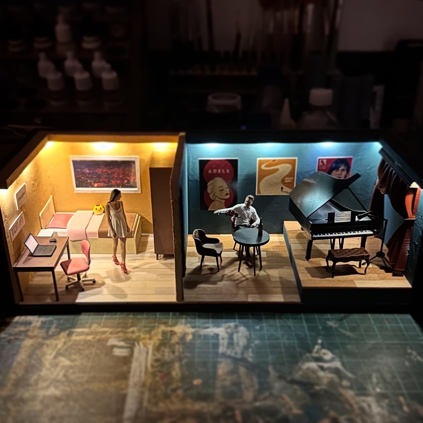 Lit miniature scene with a bedroom, a lounge and a piano stage side by side